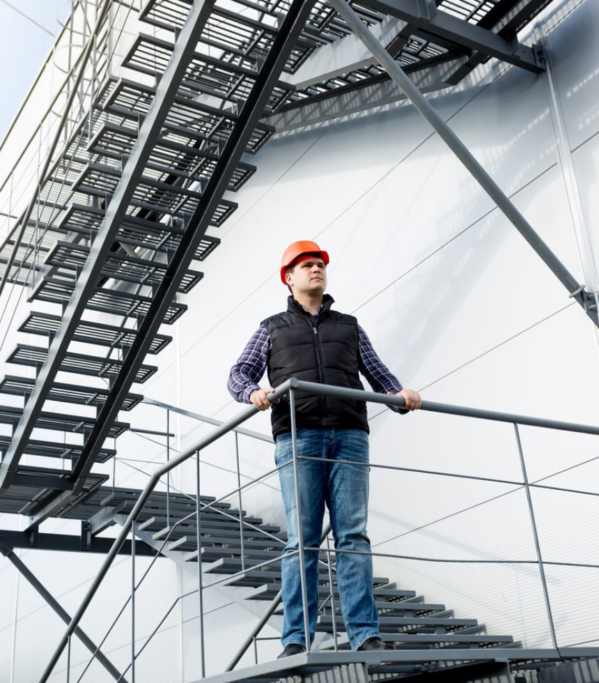 Male construction worker standing on steel staircase at factory